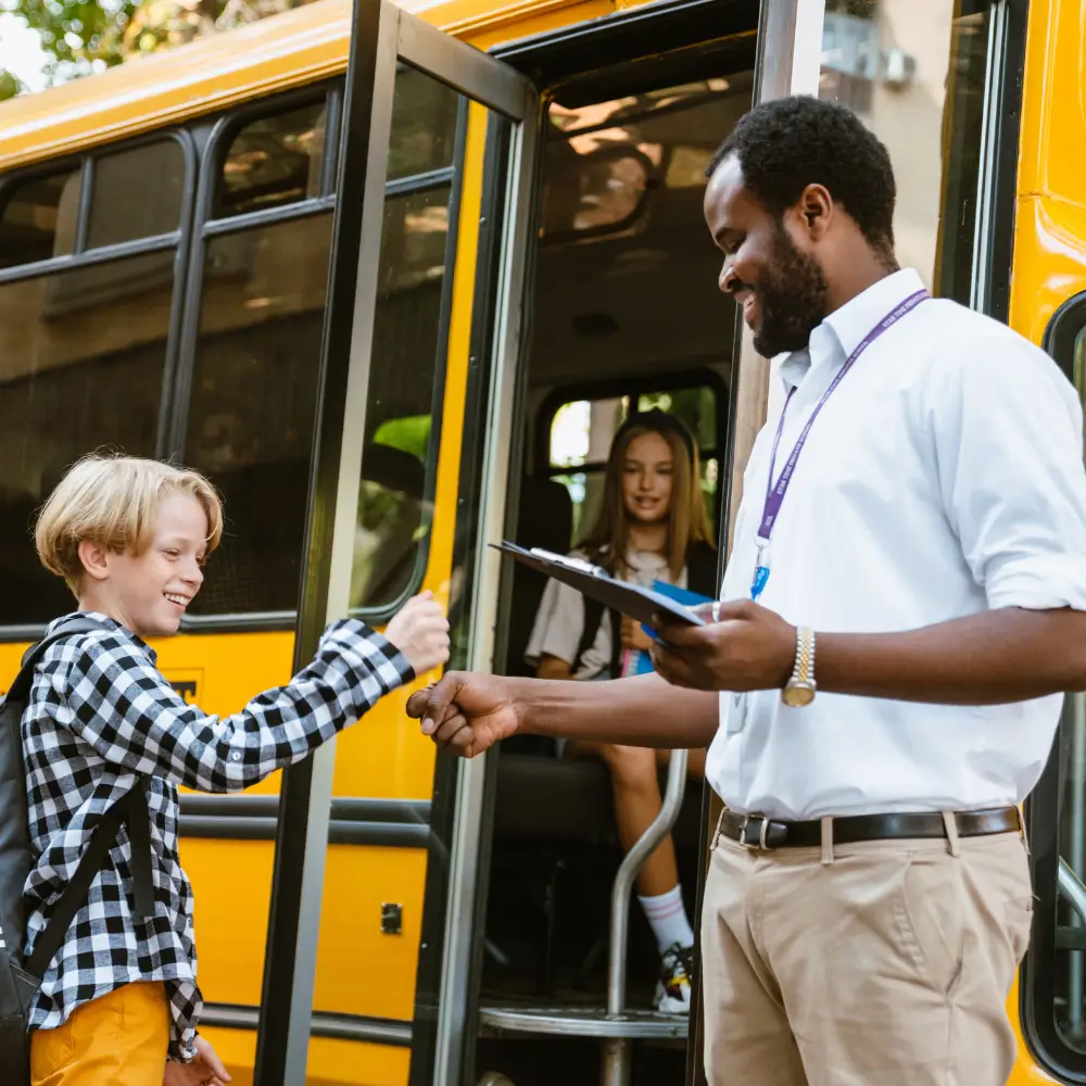 a man fist bumping a boy in front of a school bus