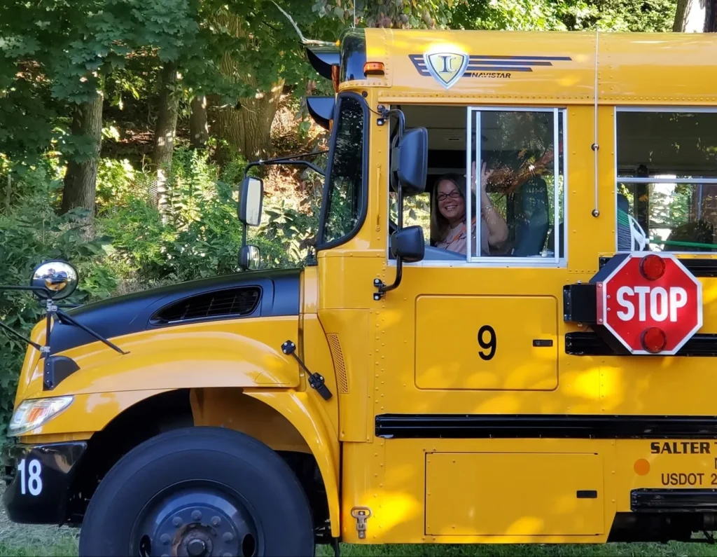 a smiling woman in the window of a school bus